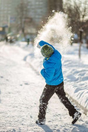 Boy in blue jacket thrown snow. Snowball was scattered for many snowflakes after throwing the boy. The snow sparkles in the sun. Sunny winter day.の写真素材