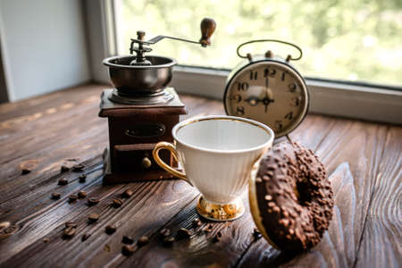 white kettle and cup on table. Breakfast by window. Chocolate donat next to scattered coffee beans.の写真素材