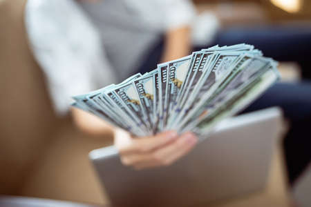 Hand holding out a bundle of fanned dollars. Payment by cash banknotes. Cash bills pouring into freelancer. Easy money earned on online exchanges or remote earnings. Return of savingsの写真素材