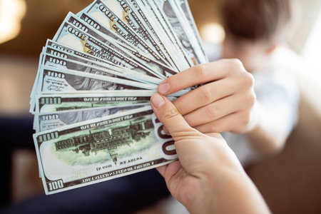Banknotes of one hundred dollars are fan-folded close-up. Hand giving money. Transfer of money from...
