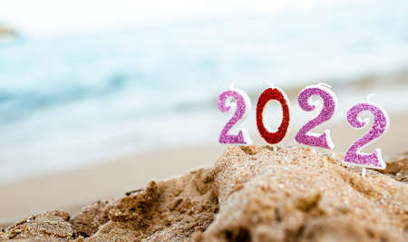 Figures 2022 against background of coastal waves by ocean or sea with caramel cane. Travel during quarantine on New Year's Eve, before arrival of new year. Celebrating the 2021 departure on beach during the Christmas holidayの写真素材