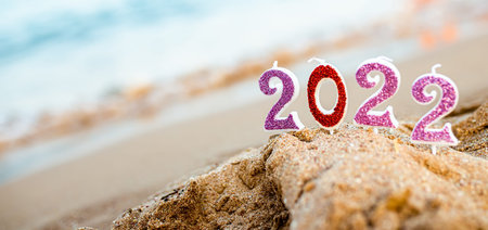 Figures 2022 against background of coastal waves by ocean or sea with caramel cane. Travel during...
