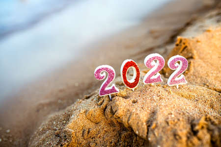 Figures 2022 against background of coastal waves by ocean or sea with caramel cane. Travel during quarantine on New Year's Eve, before arrival of new year. Celebrating the 2021 departure on beach during the Christmas holidayの写真素材