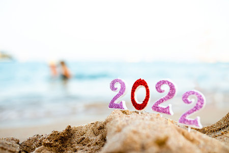 Figures 2022 against background of coastal waves by ocean or sea with caramel cane. Travel during...