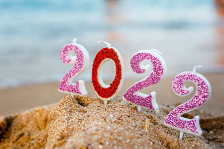 Figures 2022 against background of coastal waves by ocean or sea with caramel cane. Travel during quarantine on New Year's Eve, before arrival of new year. Celebrating the 2021 departure on beach during the Christmas holidayの写真素材