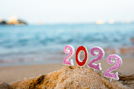 Figures 2022 against background of coastal waves by ocean or sea with caramel cane. Travel during...