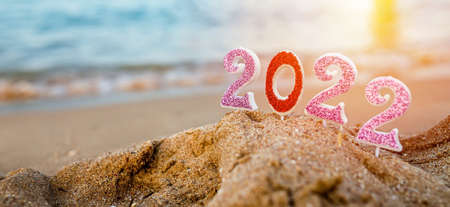 Figures 2022 against background of coastal waves by ocean or sea with caramel cane. Travel during quarantine on New Year's Eve, before arrival of new year. Celebrating the 2021 departure on beach during the Christmas holidayの写真素材