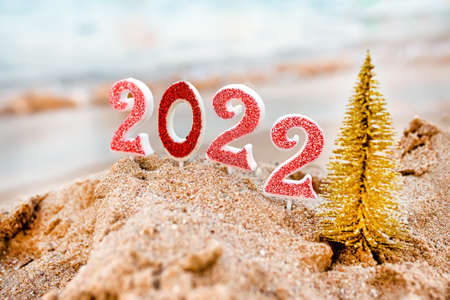 Figures 2022 against background of coastal waves by ocean or sea with caramel cane. Travel during quarantine on New Year's Eve, before arrival of new year. Celebrating the 2021 departure on beach during the Christmas holidayの写真素材
