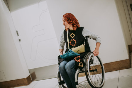 A woman in a wheelchair near washroom door with a toilet sign for people with disabilities. Public toilet in the shopping mall accessible to persons of all genders.の素材 [FY310180538380]