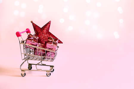 supermarket trolley with gifts packed in pink paper, a Christmas star. Colors of year 2022. pacific pink color. New Year's Eve shopping Gift Campaignの写真素材