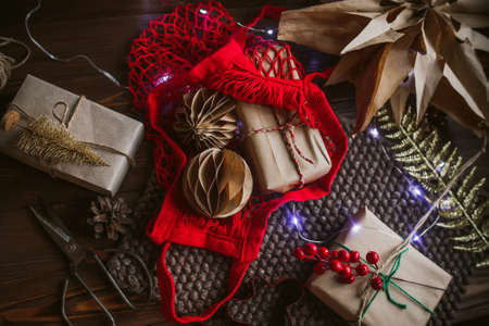 Eco shopping bag red string bag on the table with gifts in craft packaging for Christmas. Handmade craft paper christmas decorations on wooden table. New Year Eve. Selective focus.の写真素材