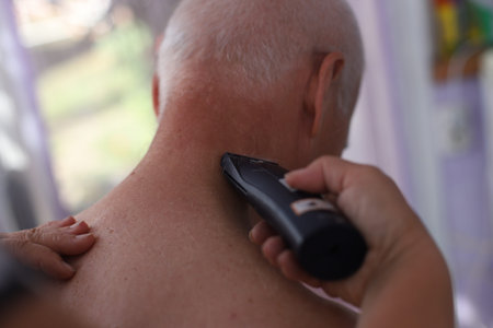 mature handsome man with short silver hair at home. Elderly man getting haircutting with electric...
