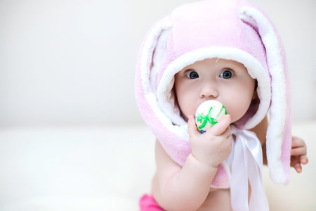 Easter concept. little girl in rabbit hat. child holds an Easter egg. Funny toddler lies and looks...