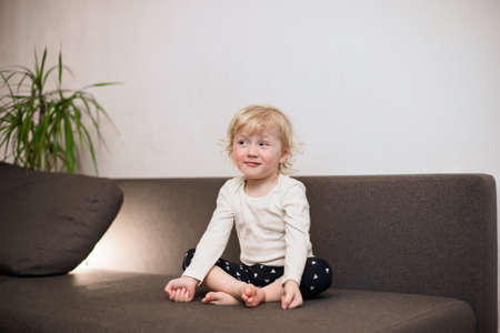 Cute little girl meditating on sofa in home. Child doing yoga exercise in lotus pose near cat.の写真素材