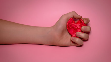 hand holds red Crumpled paper heart heart on pink background. paper heart in the palm. heart health conceptの写真素材