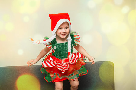 girl in santa's little elf's dress gallops in hall on couch. child in Miss Santa's hat with pigtails...