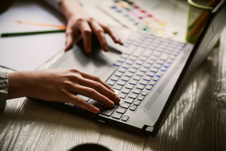 The hands of a teenage boy on a laptop keyboard. Learning to draw online. Distance courses of creativity and fine arts for teenagers and young people. Defocusedの写真素材