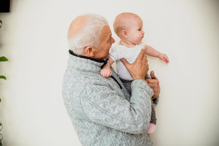 An elderly man holds his granddaughter. Happy grandfather with a little girl in his arms. End of self-isolation and meeting relatives at home in a family atmosphere for the holidays.の写真素材