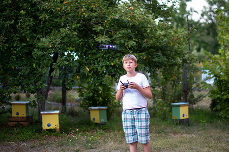 The boy looks at the launched drone. The drone flies against the backdrop of a garden in the...
