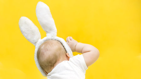 child with Easter bunny ears raised his hand. kid turned away. back of child with short blond hair on yellow background.の写真素材