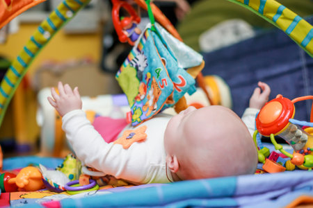 The baby lies on a developmental mat and flips through a textile educational book with the image of animals. The child learns about the world and learns shapes and colors while playing. Defocusedの写真素材