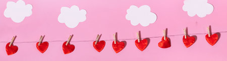 A row of red hearts on clotheslines on a pink background with clouds. paper crafting. Background for Valentine's Day or Women's Day.の写真素材