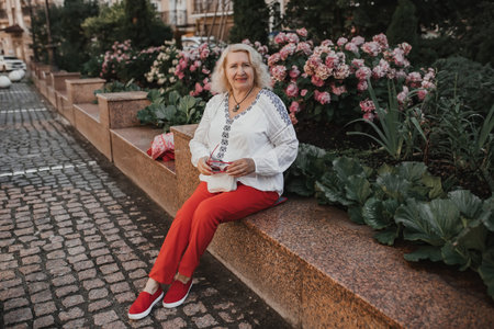 An elderly woman sits near azaleas in the city while traveling or walking.