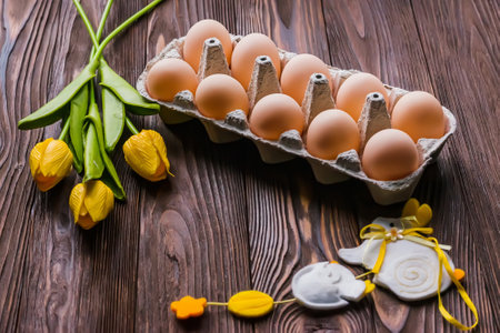 Cardboard tray with Easter eggs on a wooden table next to a bouquet of yellow tulips and Easter decorの写真素材