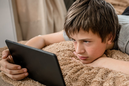 guy with tablet lies on the bed in children's room and watches educational videos in a distance...