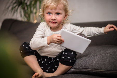 a girl who gets off the sofa with a tablet in her hands, but she does it carelessly and can break it. The girl does not notice the risks associated with unqualified handling of an electronic device.の写真素材