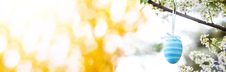 Easter background with a blue Easter egg on a branch of bird cherry that blooms with white flowers on Easter day in springの写真素材
