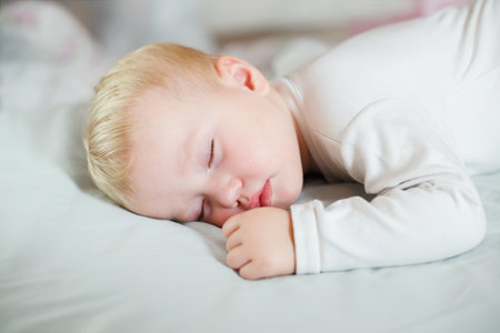a child rests during a daytime nap at home with a pen with a fist next to his face. Baby girl sleeps on his stomach.の写真素材