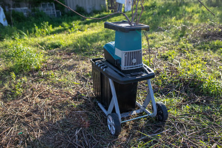 garden shredder was turned on in the net on the lawn next to a pile of dry branches that after remained pruning the garden during the spring workの写真素材