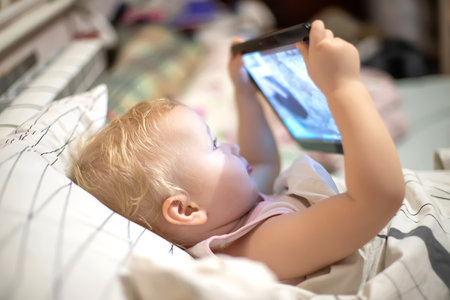 sick child in bed looks at screen of tablet computer. child is studying online at home. Entertaining children during lockdown.の写真素材