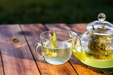 cup of hot linden tea with spoon and linden flowers on wooden table in a gardenの写真素材