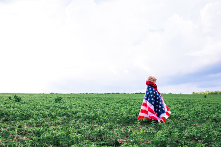 Patriotic Holiday. cute little child girl with american flag. USA celebrate 4th of July enjoying sunset on nature. independence day concept.の写真素材