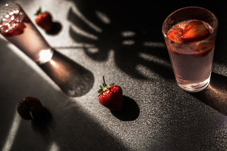 Summertime strawberry cocktail. A refreshing mix of strawberries, ice cubes, and a touch of mint. glass on a dark backdrop, perfect for a party or a relaxing evening.の写真素材