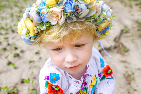 A sad Ukrainian girl in a wreath and embroidered shirt. The child is a refugee from Ukraine. Girl who lost her homeの写真素材