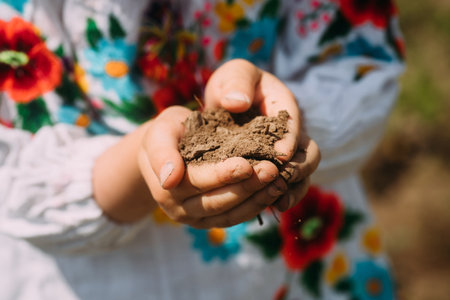 hands of Ukrainian girl holding breast of Ukrainian land in hands. Ukrainians lost homes and land. A piece of the homeland in the hands. Unhappy children of Ukraine in emigration. Refugee Dayの写真素材