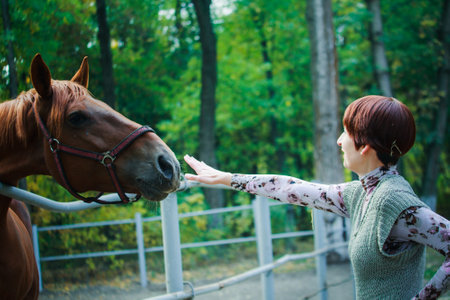 A woman is afraid of a horse. The woman reached out her hand to the muzzle of the horse. The horse reaches for food in the womans hand. Horse race in the forest.の写真素材
