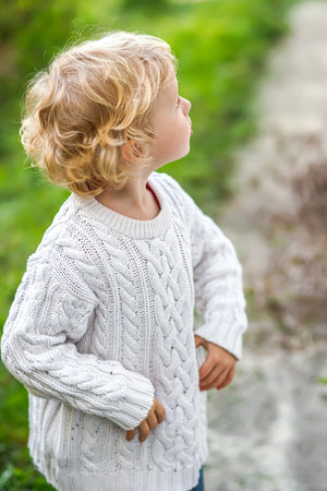 A little girl in a white sweater looks up in surprise. Children's emotions. Portrait of a little 4-year-old girl with curly white hairの写真素材
