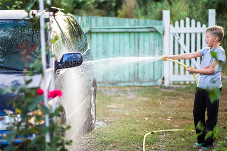 Car wash at home. Boy earns pocket money by washing cars with a hoseの写真素材