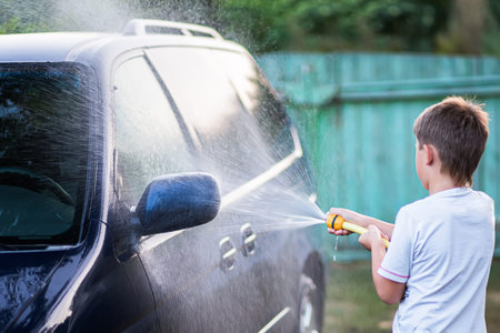 boy having fun washing the car. child washes the hood of a car with water from a garden hoseの写真素材