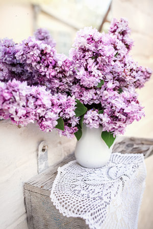 Bouquet of purple lilac in white ceramic vase on woven napkin near vintage mirror Home decor with fresh flowers.の写真素材