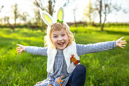 A happy little girl put on Easter bunny ears and spread her arms out to the sides rejoicing during a...