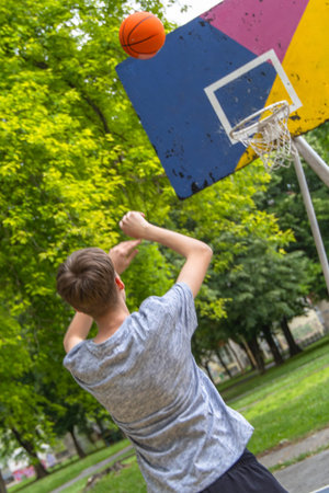Teenager Watches Basketball Go Through Hoop On Outdoor Court