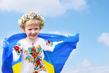 Yellow blue Ukrainian flag in hands of girl running on mangled field of wheat. Happy child with the flag of Ukraine. Independence Day. Flag Day. Constitution day.の写真素材