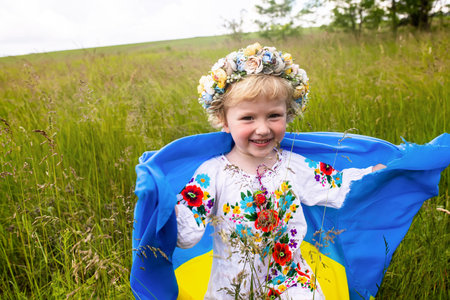 Yellow blue Ukrainian flag in hands of girl running on mangled field of wheat. Happy child with the flag of Ukraine. Independence Day. Flag Day. Constitution day.の写真素材
