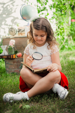 Girl reading with magnifying glass in garden. Back to Schoolの写真素材