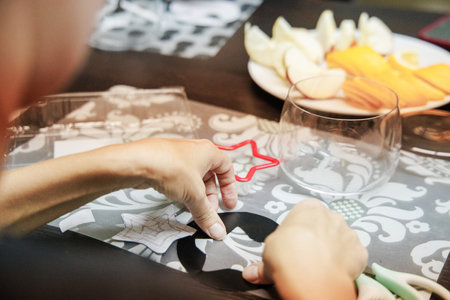 A person is engaged in a craft, using cookie cutters on a patterned surface, surrounded by a colorful fruit platter for a delightful snack.の写真素材